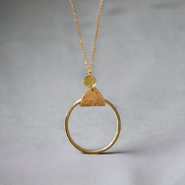 Collier fin dorée avec pendentif grand anneau créole attaché par une fine pièce de liège brut, sur fond gris