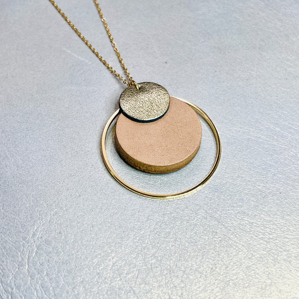 NUNE collier doré fin Danaé avec pendentif rond en cuir recyclé doré satiné, sur fond beige doré. Vue de biais