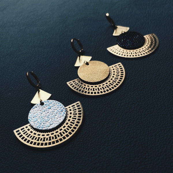 Boucles d'oreilles dorées Nune modèle Ephésia en cuir bleu ciel métal patiné, doré satiné et noir grainé irisé sur fond noir