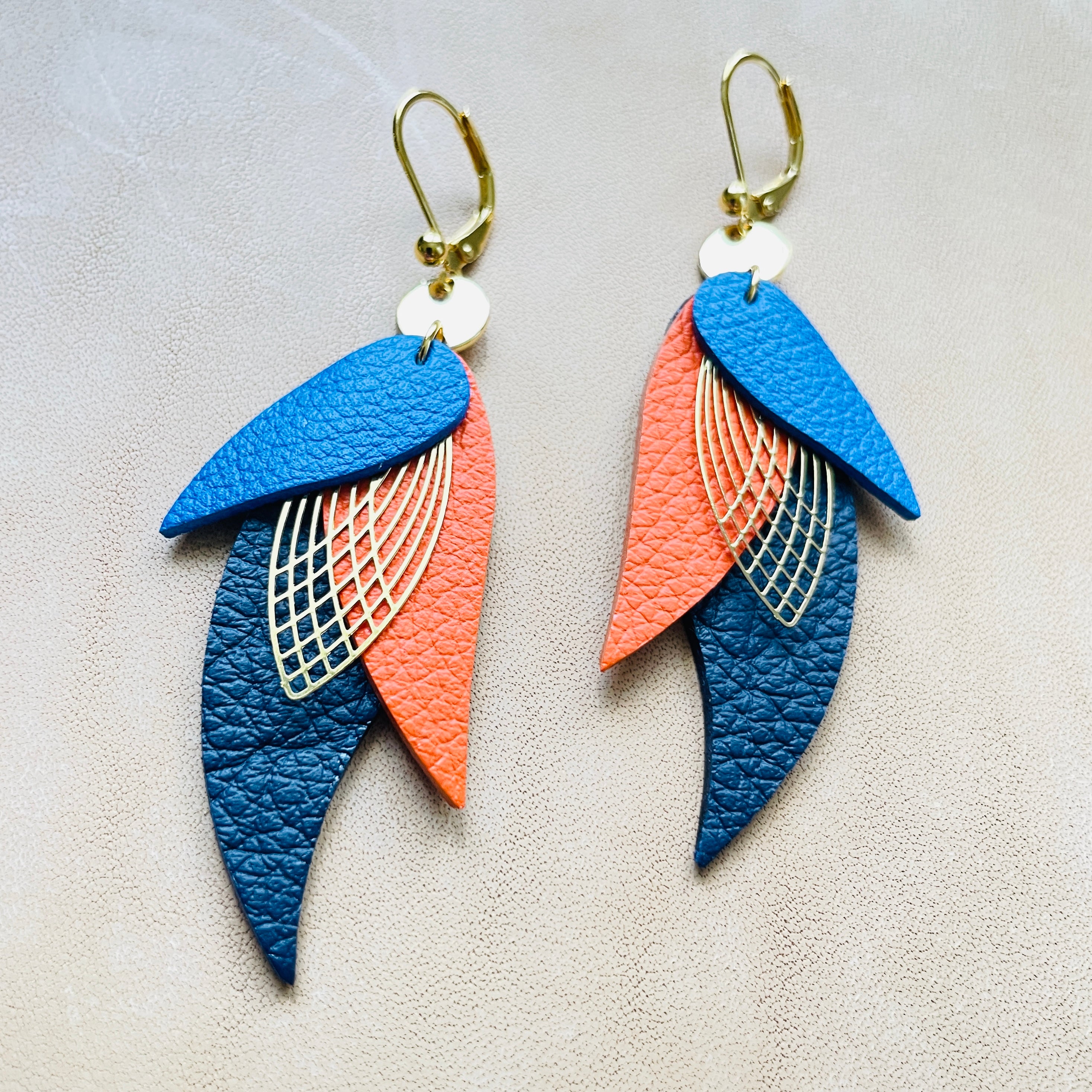 boucles d'oreilles dorées Nune modèle Ara en plumes de  cuirs bleu roi grainé, carotte grainé et bleu mariné grainé sur cuir beige