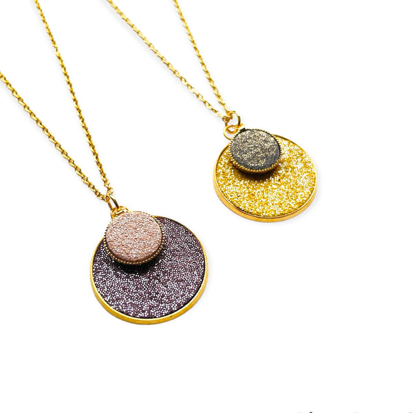 Deux Colliers Bulles pailletées Nune, court doré avec pendentif rond composé de doubles sertis de cuirs pailletés mauve et rose, et safran et gris, sur fond blanc
