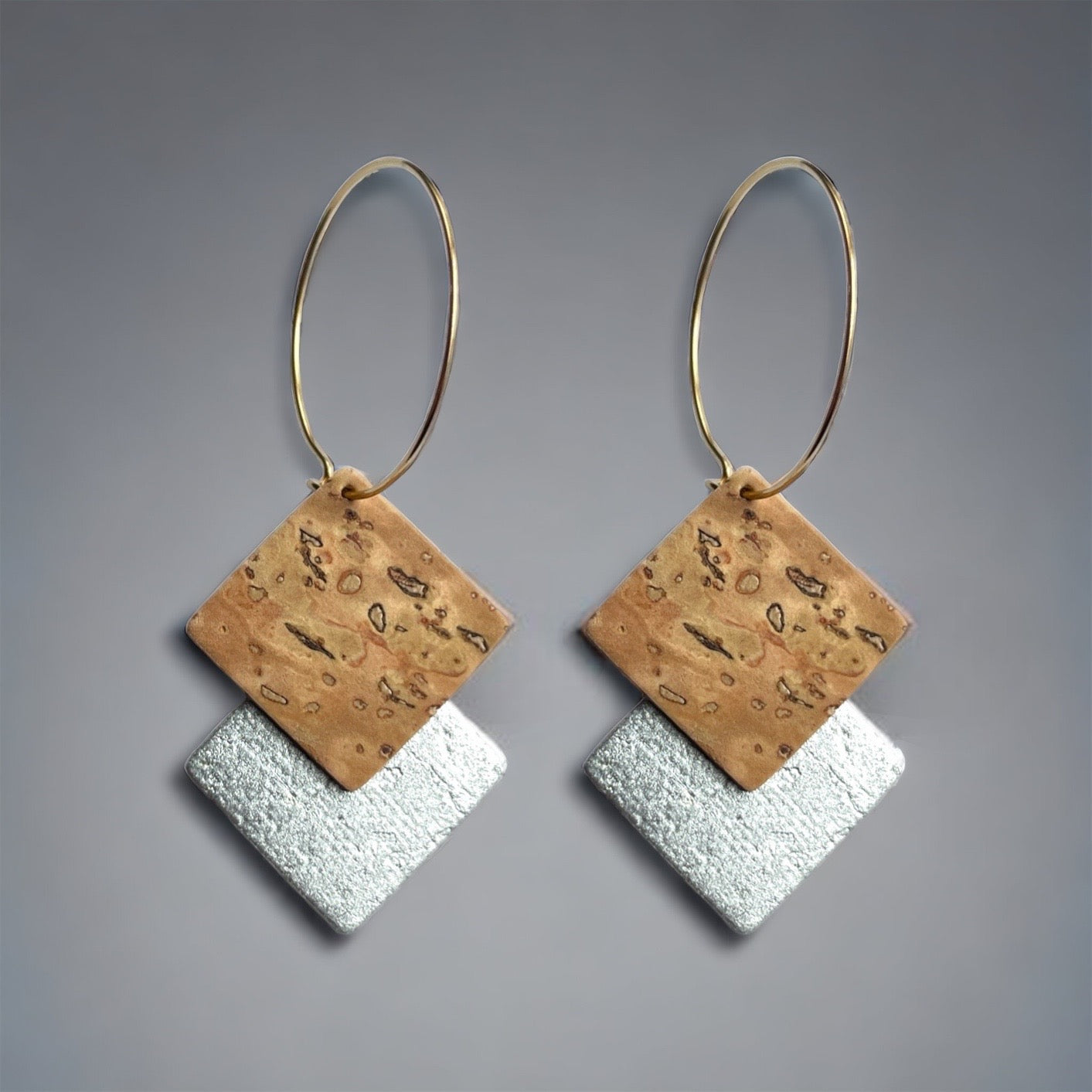 Boucles d'oreilles créoles dorées en liège brut et argenté. Forme géométrique double-losanges imbriqués, sur fond gris