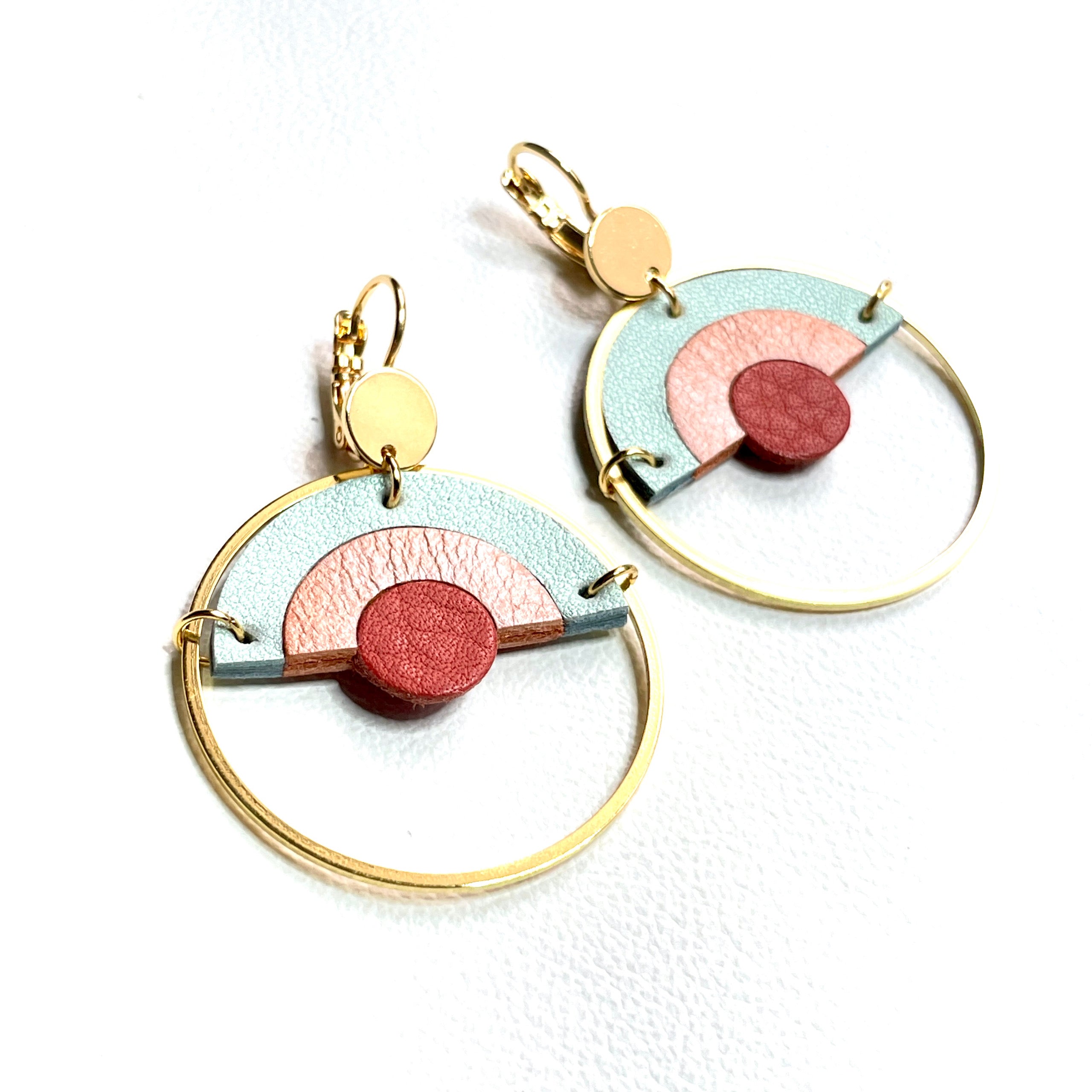 Boucles d'oreilles dorées et rondes, modèle Sunset de la marque Nune, avec un dégradé arc-en-ciel de cuirs rose incarnat, corail nacré clair et bleu lune nacré, sur fond blanc