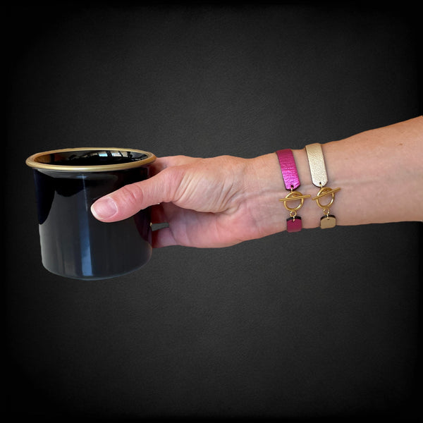 2 bracelets en cuir double face bicolores, avec fermoir boucle dorée en T, en cuirs fushia métallisé pour le 1er, et doré antique mat  pour le second, portés au poignet et vus de dessous