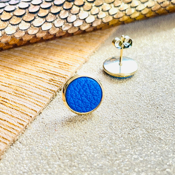 Puces d'oreilles dorées rondes Nune modèle Ilis avec cuir bleu roi grainé, sur fond de cuirs beige