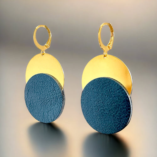 Boucles d'oreilles dorées Nune modèle Eclipse avec disque de cuir bleu nuit sur un disque doré, sur fond gris doré 