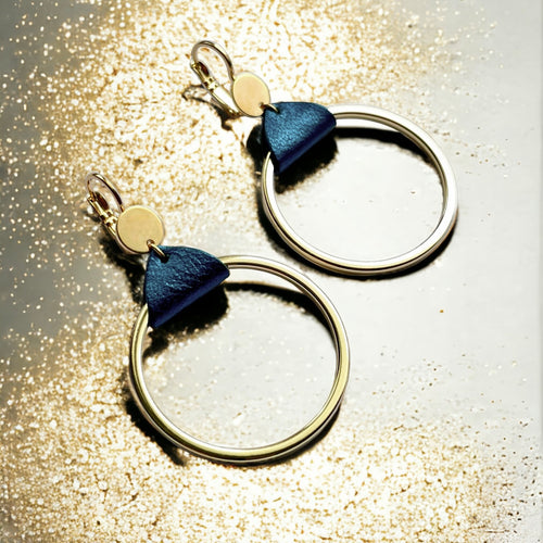 Boucles d'oreilles dorées, grands anneaux créoles, noués par un morceau de cuir bleu nuit métallisé aux accroches dormeuses, présentées sur fond doré pailleté