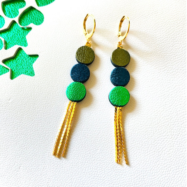 Longues et fines boucles d'oreilles Nune à franges dorées avec 3 petits disques de cuir recyclé kaki métallisé, bleu nuit métallisé et vert métallisé, sur fond blanc et vert étoilé. Modèle Janis