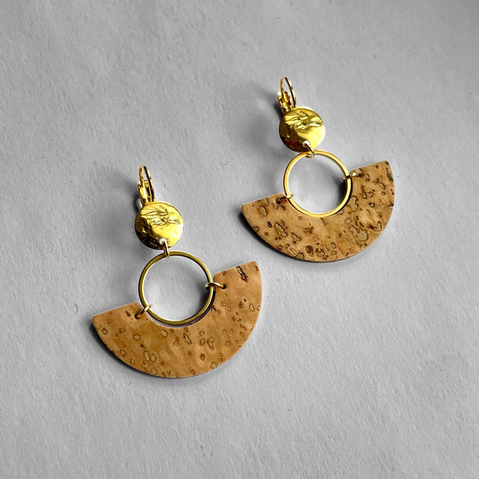 paire de boucles d'oreilles dorées en forme de demi-lunes en liège brut, sur fond gris