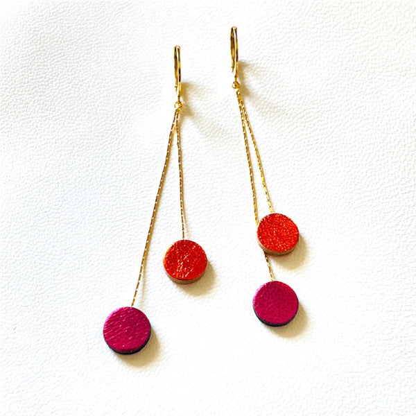 Longues et fines boucles d'oreilles Nune dorées terminées petits disques de cuir recyclé orange sanguine métallisé et fushia métallisé, sur fond blanc. Modèle Merry
