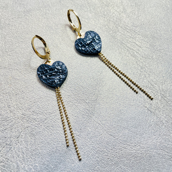 NUNE fines boucles d'oreilles dorées, petits cœurs de cuir recyclé noir brillant façon serpent et chaînettes, sur fond gris
