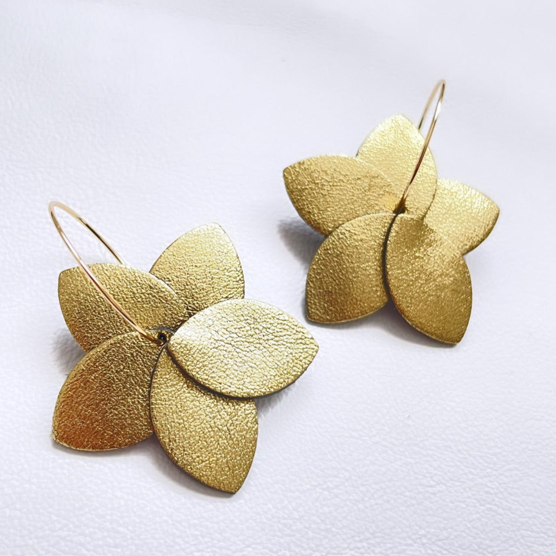 Nune boucles d'oreilles créoles Tiara en cuir doré satiné et anneaux dorés, sur fond blanc