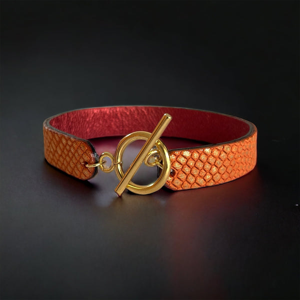 Bracelet en cuir double face bicolore, avec cuir rubis métallisé au verso et cuir orangé or façon croco au recto avec fermoir boucle dorée en T, sur fond noir