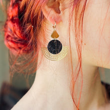 Charger l&#39;image dans la galerie, boucle d&#39;oreille dorée Nune modèle Ephésia en cuir noir grainé irisé portée par un modèle aux cheveux rouges et au teint pâle
