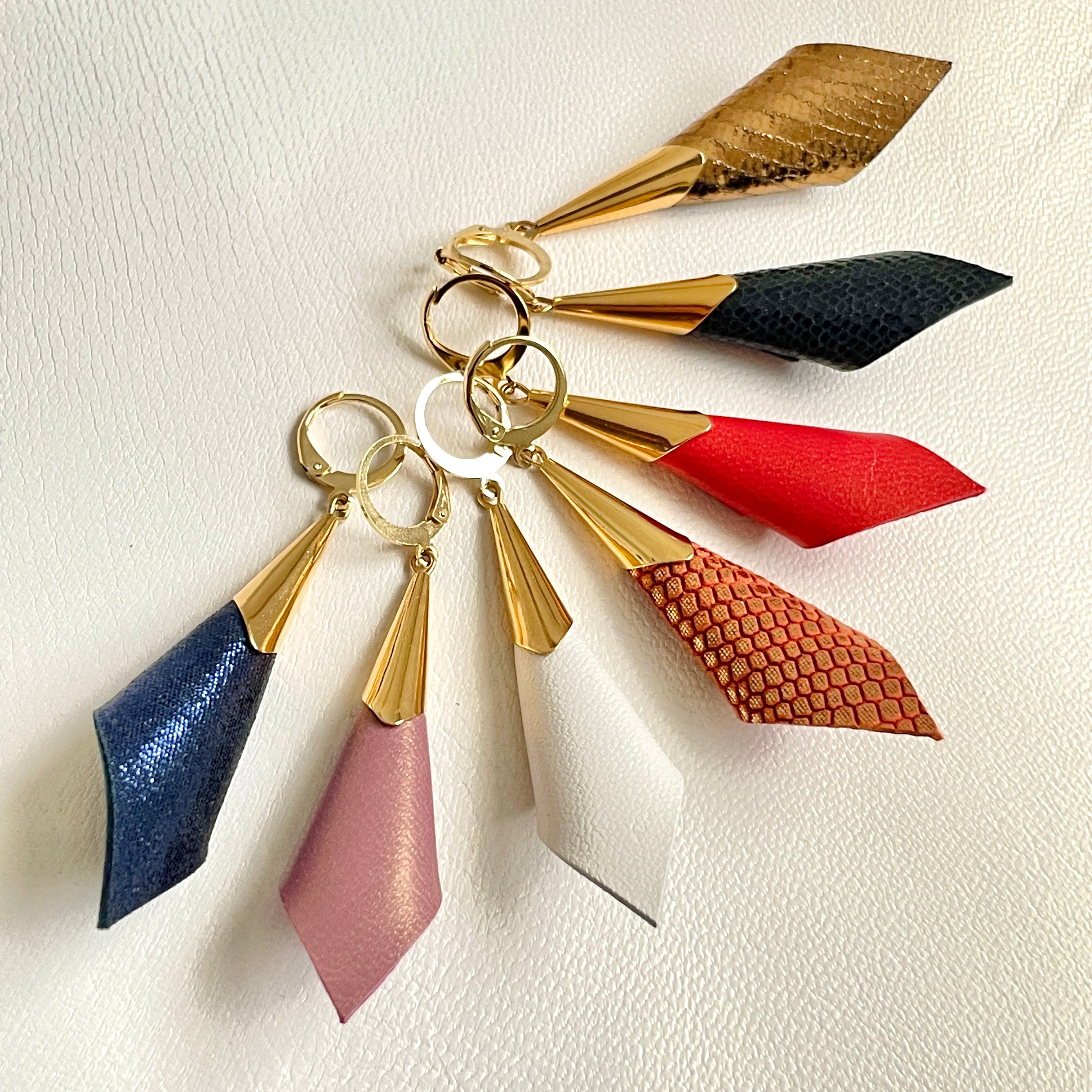 Boucles d'oreilles dorées Nune modèle Alice en forme de cônes de cuirs de 7 couleurs différentes , sur fond cuir blanc cassé nacré