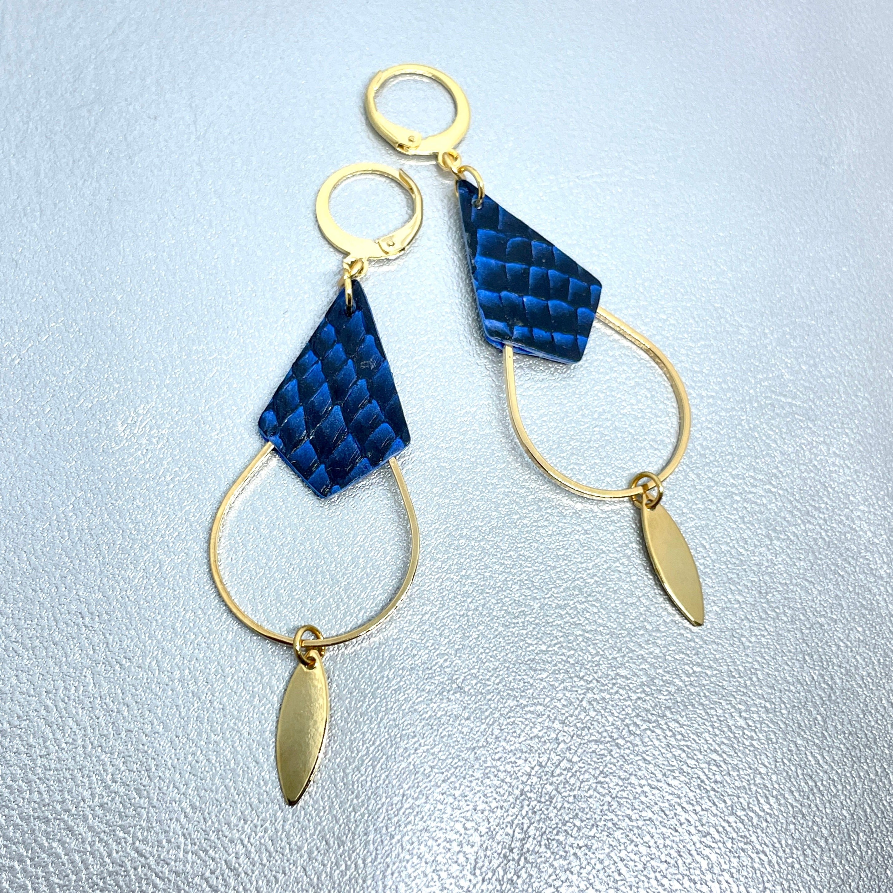 Boucles d'oreilles Gali de Nune, dorées à l'or fin avec triangle de cuir marin, cuir de poisson saumon bleu saphyr écaille, de forme grande goutte, sur fond cuir gris argenté
