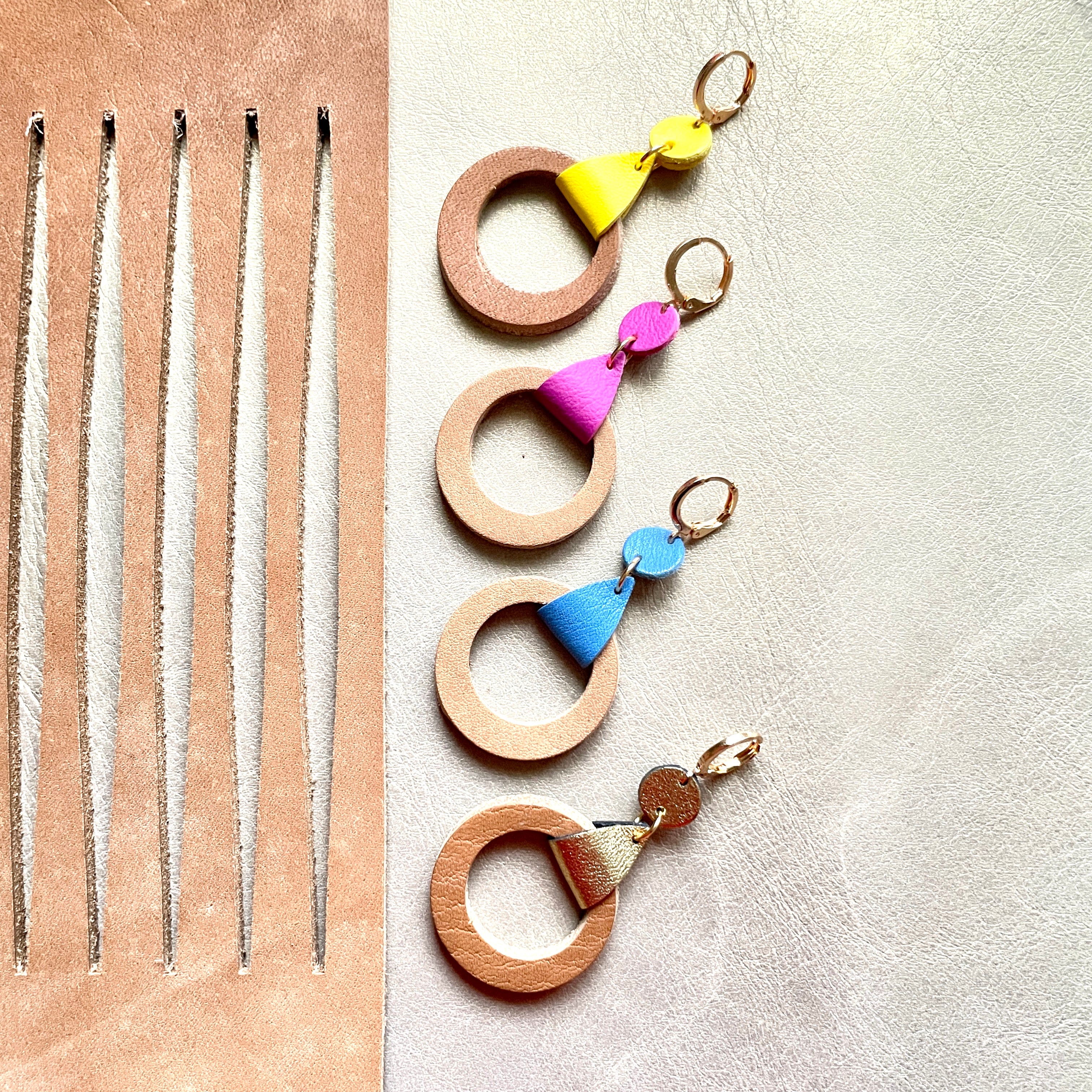 4 boucles d'oreilles dorées Nune modèle Cyllène en cuirs beige amande et doré satiné, bleu denim mat, mauve mat, jaune citron sur fond gris doré