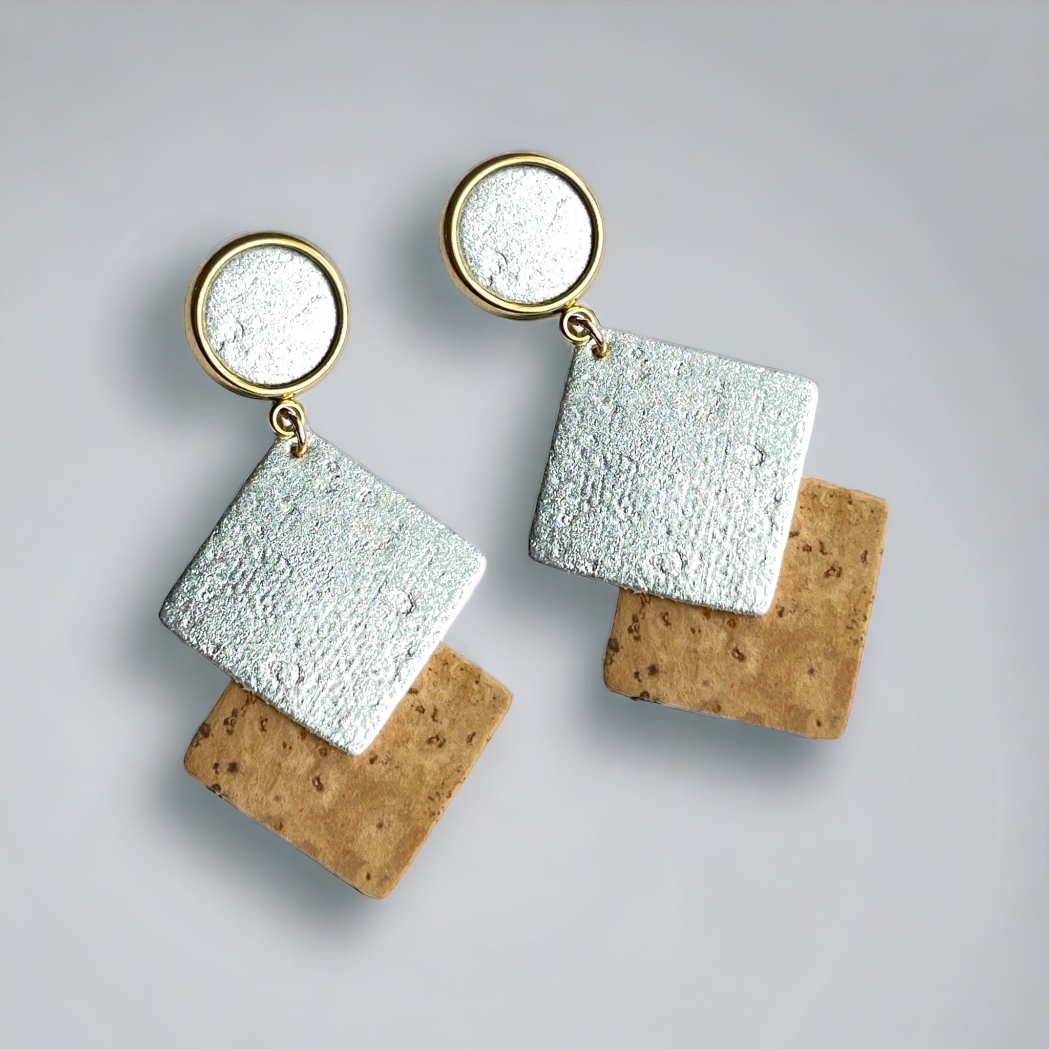 Boucles d'oreilles dorées avec puces cabochon et duo de losanges en liège brut et argenté, sur fond gris