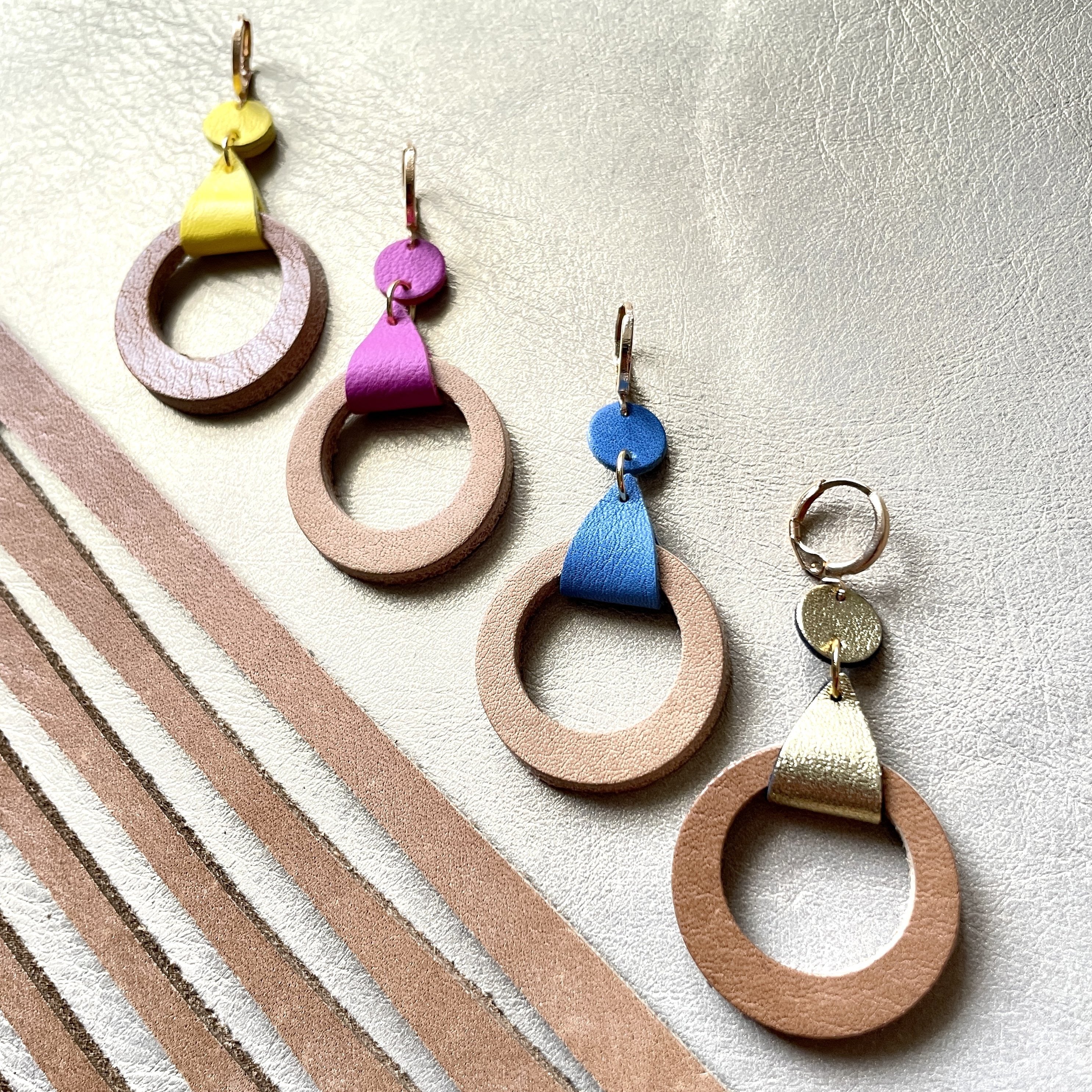 boucles d'oreilles dorées Nune modèle Cyllène en cuirs beige amande et doré satiné, bleu denim mat, mauve mat, jaune citron sur fond gris doré