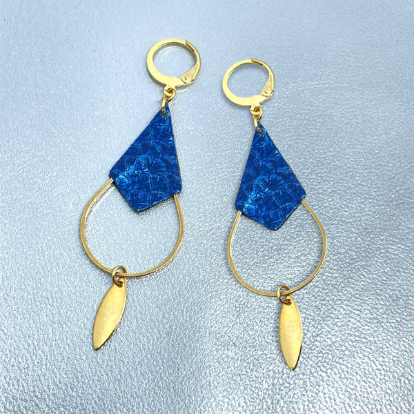 Boucles d'oreilles Gali de Nune, dorées à l'or fin avec triangle de cuir marin, cuir de poisson saumon bleu saphir métallisé, de forme grande goutte, sur fond cuir gris argenté