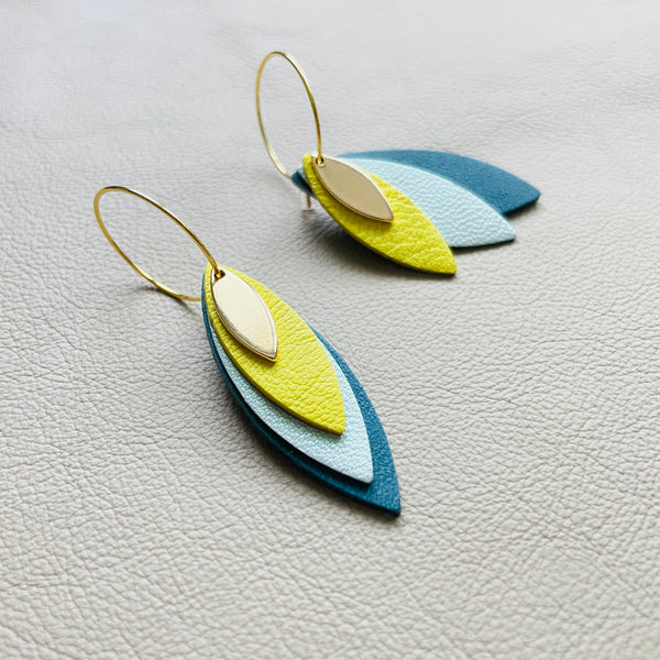 Boucles d'oreilles créoles dorées Nune modèle Piume en cuirs jaune citron, bleu lune nacré et vert paon sur fond gris