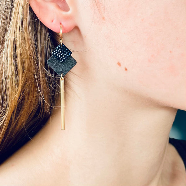 boucle d'oreille dorée Nune modèle Ada en cuirs noir grainé et noir grainé irisé portée par un modèle aux cheveux blonds et au teint pâle