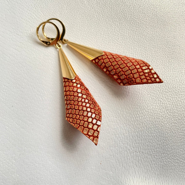 Boucles d'oreilles dorées Nune modèle Alice en forme de cônes de cuir orangé or façon serpent, sur fond cuir blanc cassé nacré