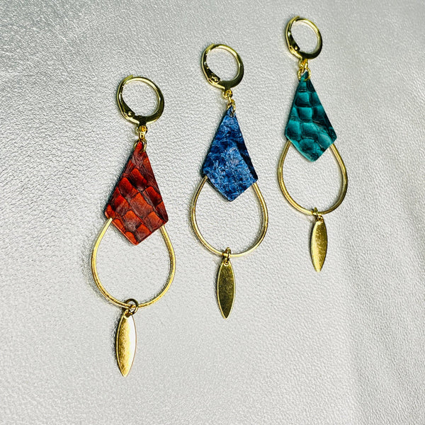 Boucles d'oreilles Gali de Nune, dorées à l'or fin avec triangles de cuirs marins, cuirs de poisson saumon rouge carmin écaille, bleu saphyr métallisé et vert émeraude écaille, de forme grande goutte, sur fond cuir gris argenté