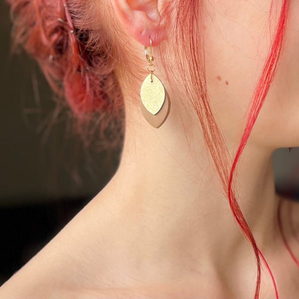 boucle d'oreille dorée Nune modèle Phylla en cuirs beige amande et doré satiné portée par un modèle aux cheveux rouges et au teint pâle