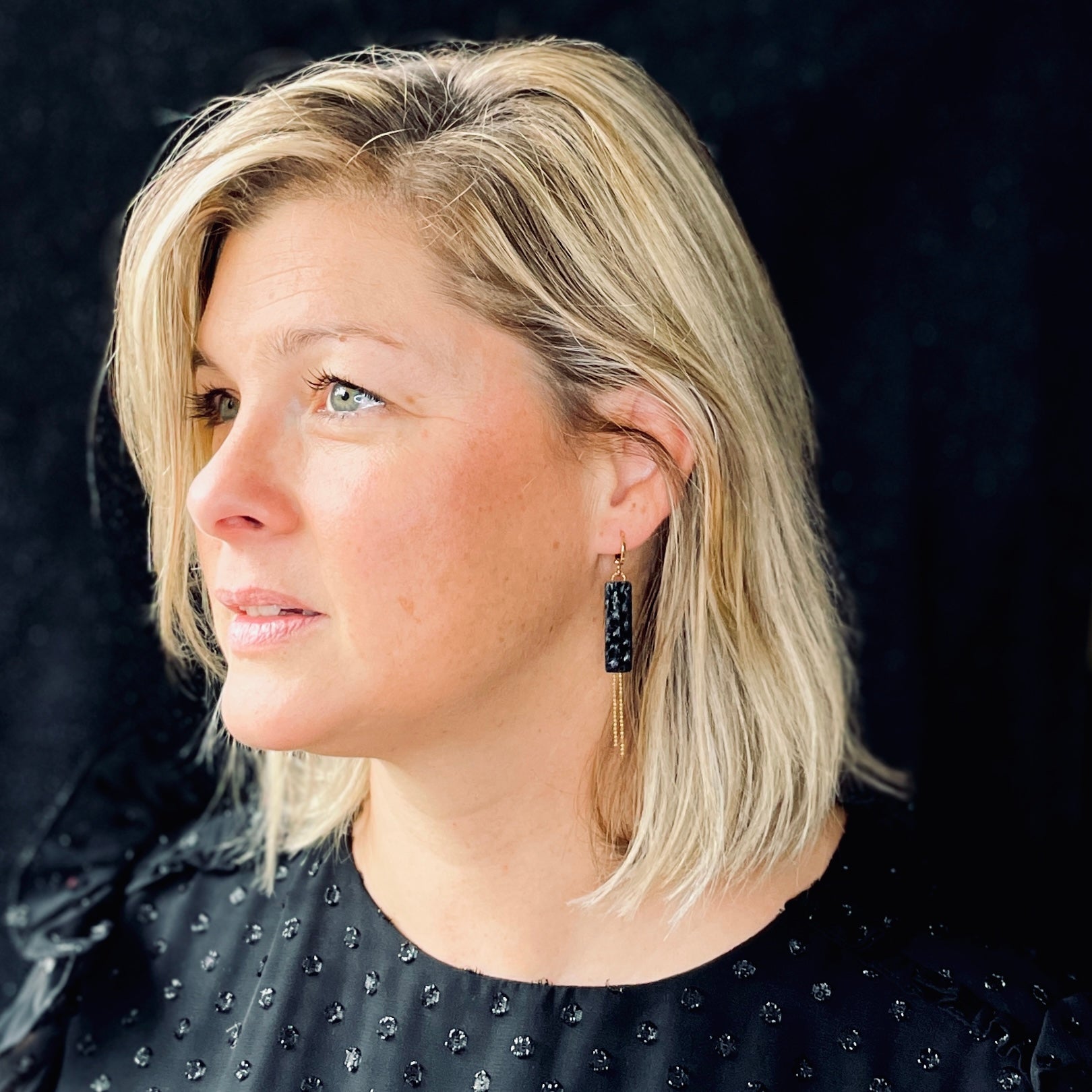 Boucle d'oreille Effinis de Nune, dorée à l'or fin avec cuir marin, cuir de poisson saumon noir d'encre, de forme effilée avec chaînettes dorées pendantes, portée à l'oreille