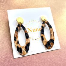 Charger l&#39;image dans la galerie, Puces d&#39;oreilles dorées Drys de la marque Nune, avec leurs anneaux ovales en cuir léopard, sur fond cuir mauve nacré, vues de haut
