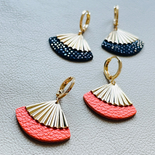 Petites boucles d'oreilles dorées Nune modèle Alya avec sequin éventail et pièces de cuir carotte grainé et noir grainé irisé, sur fond cuir beige