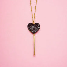 Charger l&#39;image dans la galerie, NUNE collier doré Félicie en forme de clé des cœurs cœur en cuir recyclé noir brillant façon serpent sur fond rose pastel
