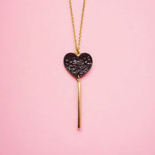 NUNE collier doré Félicie en forme de clé des cœurs cœur en cuir recyclé noir brillant façon serpent sur fond rose pastel