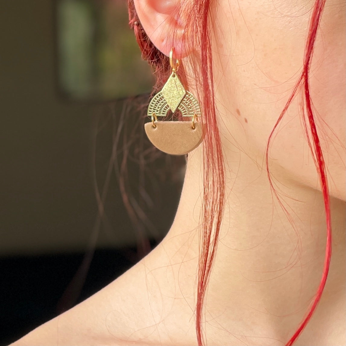 boucle d'oreille dorée Nune modèle Echo en cuirs beige amande et doré satiné portée par un modèle aux cheveux rouges et au teint pâle