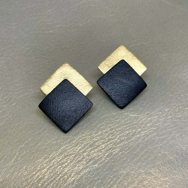NUNE boucles d'oreilles puces Adalis, duo de losanges en cuir recyclé noir satiné et doré clair, sur fond gris irisé