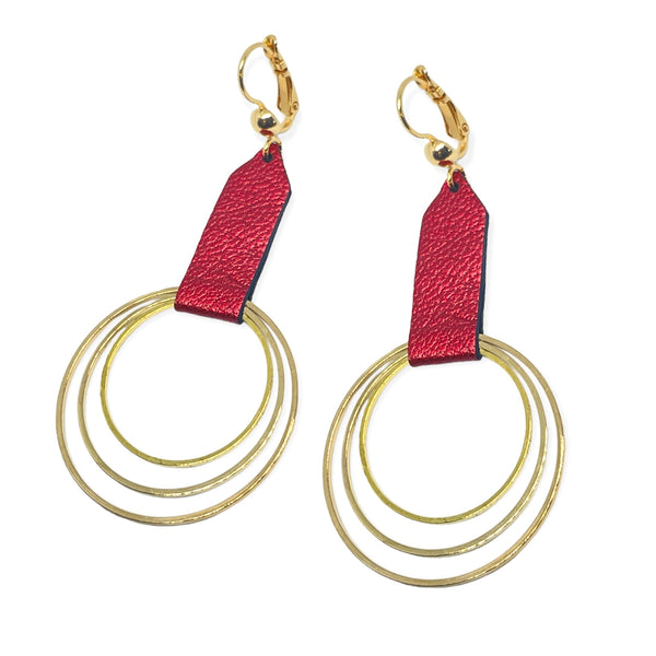 Grandes boucles d'oreilles dorées avec pendentifs en anneaux concentriques attachés par des rubans de cuir recyclé rubis métallisé, sur fond blanc. Modèle Dizzo