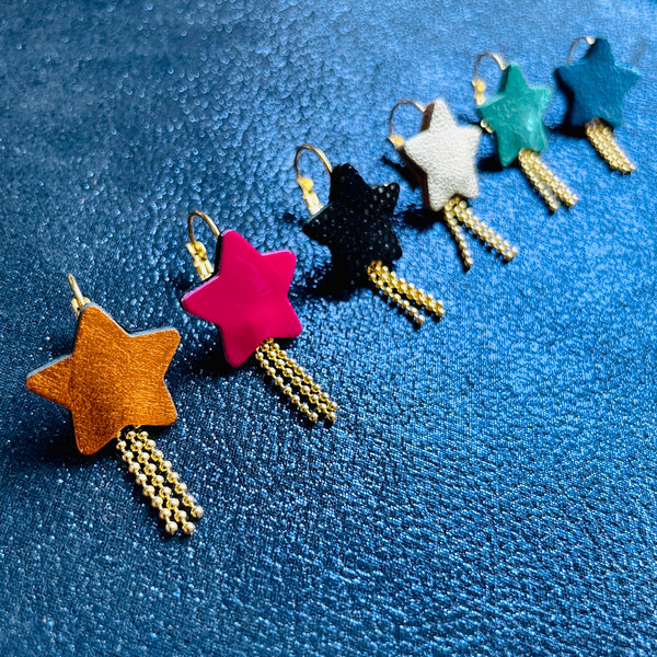 Rangée de boucles d'oreilles dorées Nune modèle Stella en forme d'étoiles, de différents coloris de cuirs recyclés : orange métallisé, rose fushia vernis, noir grainé irisé, argent, vert émeraude brillant, bleu roi métallisé