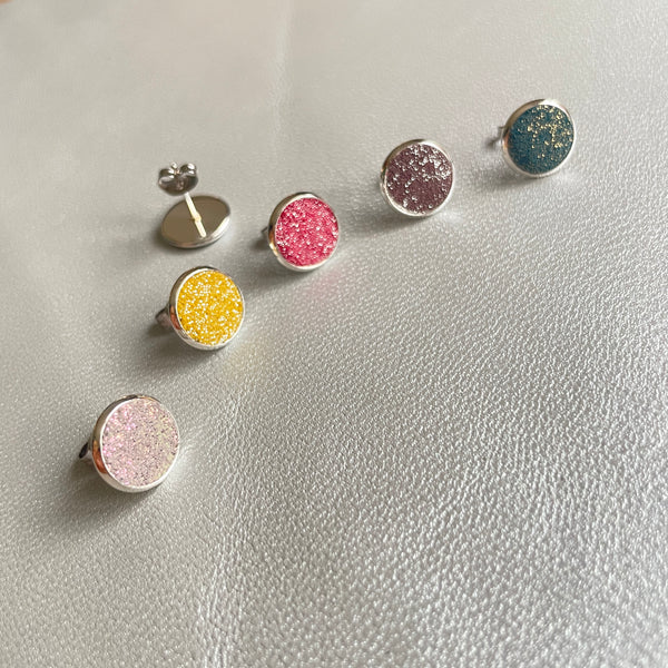 Puces d'oreilles argentées rondes Nune modèle Ilis argenté pailleté dans 5 coloris de cuirs gris pailleté irisé, safran pailleté argent, framboise pailletée argent, parme pailleté argent et vert canard pailleté or, sur fond de cuir gris métallisé