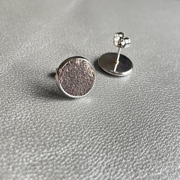 Puces d'oreilles argentées rondes Nune modèle Ilis argenté pailleté avec pastilles de cuir gris pailleté irisé, sur fond de cuir gris métallisé