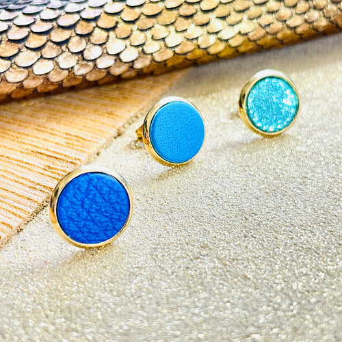 Puces d'oreilles dorées rondes Nune modèle Ilis dans 3 coloris de cuirs bleu roi grainé, bleu turquoise et vert émeraude brillant intense, sur fond de cuirs beige