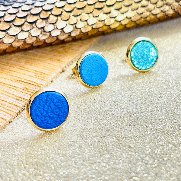 Puces d'oreilles dorées rondes Nune modèle Ilis dans 3 coloris de cuirs bleu roi grainé, bleu turquoise et vert émeraude brillant intense, sur fond de cuirs beige