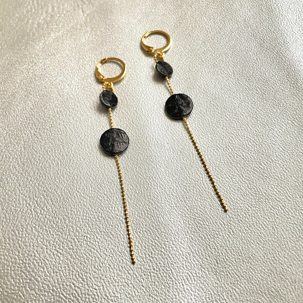 Fines boucles d'oreilles Lyre de Nune, dorées à l'or fin avec petites pastilles de cuir marin, cuir de poisson saumon noir d'encre sur chaînette dorée, sur fond gris argenté