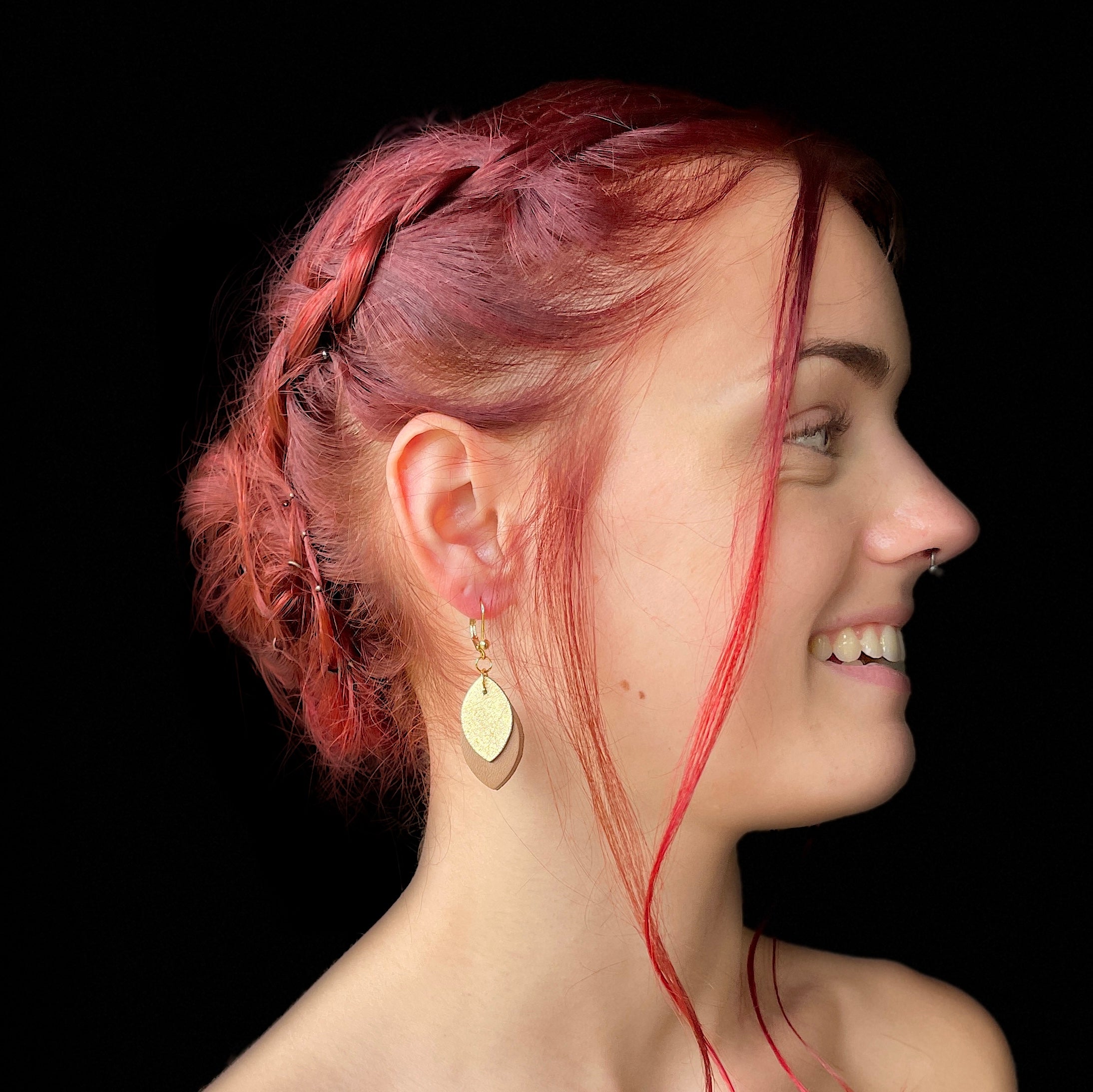 boucles d'oreille dorée Nune modèle Phylla en cuirs beige amande et doré satiné portée par un modèle de profil aux cheveux rouges et au teint pâle