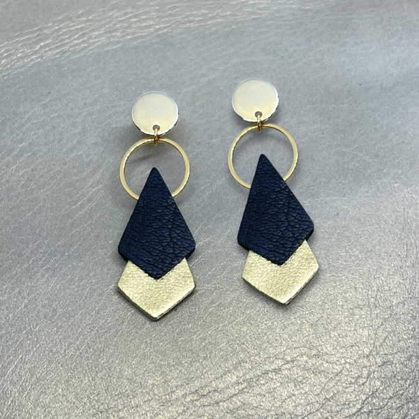 NUNE puces d'oreilles dorées Sagittis, pendentifs en duo de losanges en cuir recyclé noir et doré, sur fond beige doré