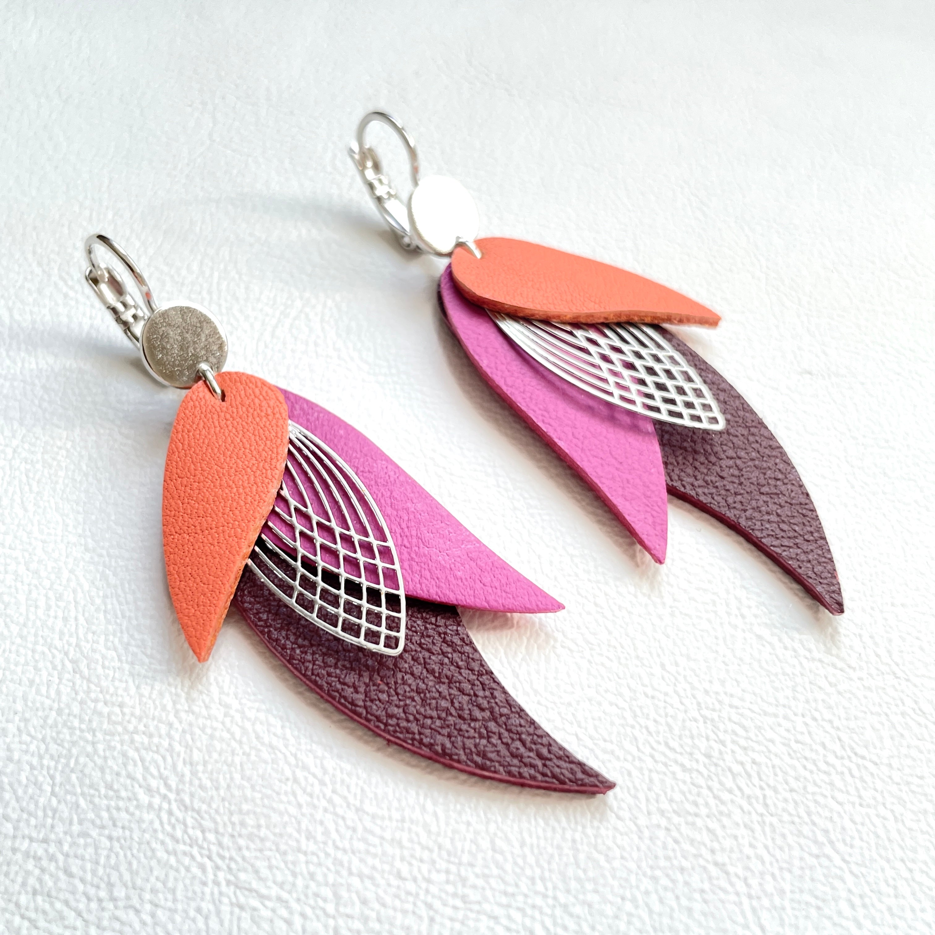Boucles d'oreilles argentées Nune en forme de plumes, modèle Ara en cuirs saumon clair, mauve et grenat grainé sur fond cuir blanc
