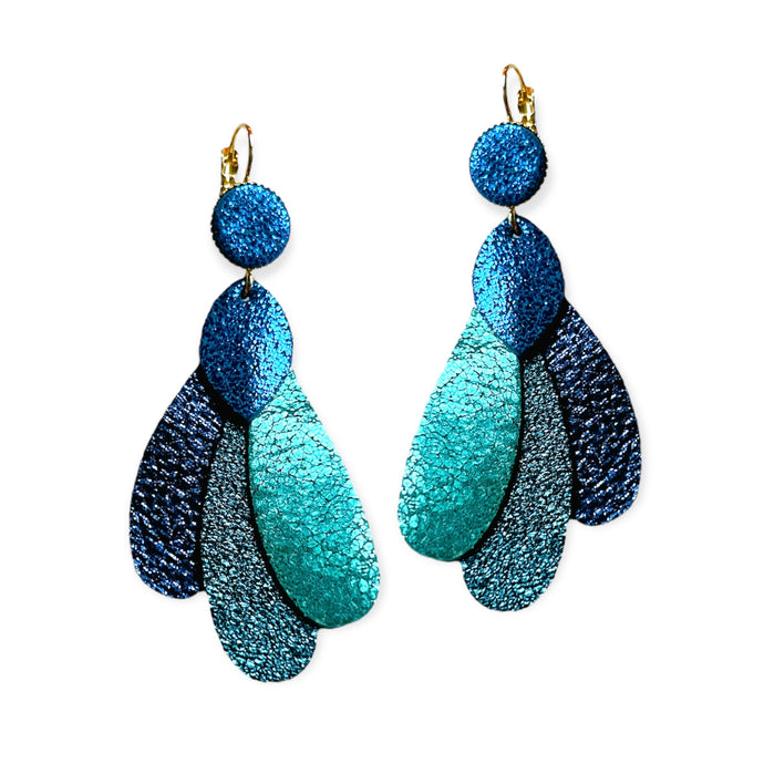 Paire de grandes boucles d'oreilles dorées en forme de plumes de paon, en cuirs recyclés bleu roi métallisé, vert émeraude brillant intense, bleu paon pailleté et bleu marine pailleté, sur fond blanc. Modèle Paon de Nune.