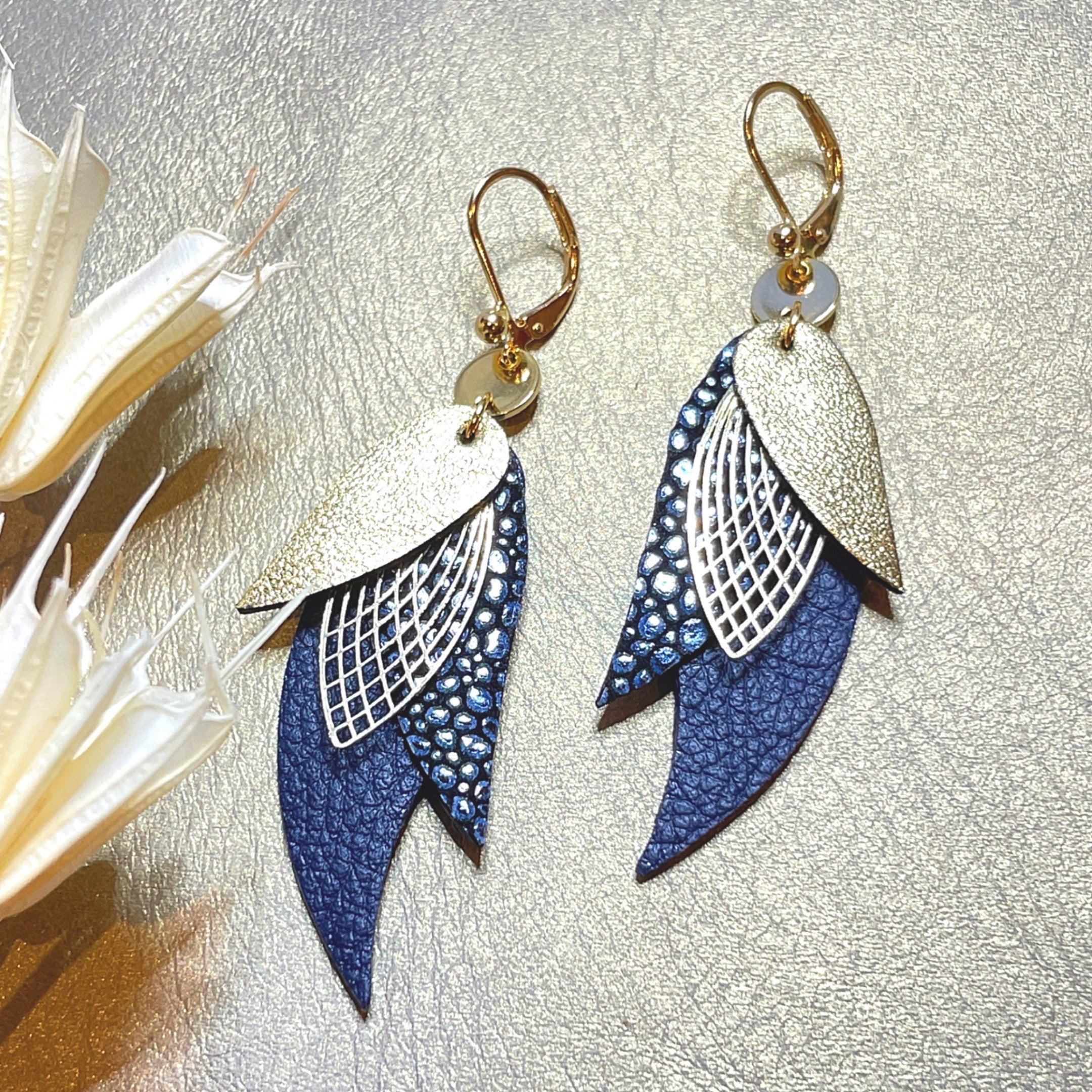 boucles d'oreilles dorées Nune modèle Ara en plumes de  cuir doré satiné, bleu nuit grainé irisé et bleu mariné grainé sur cuir beige doré