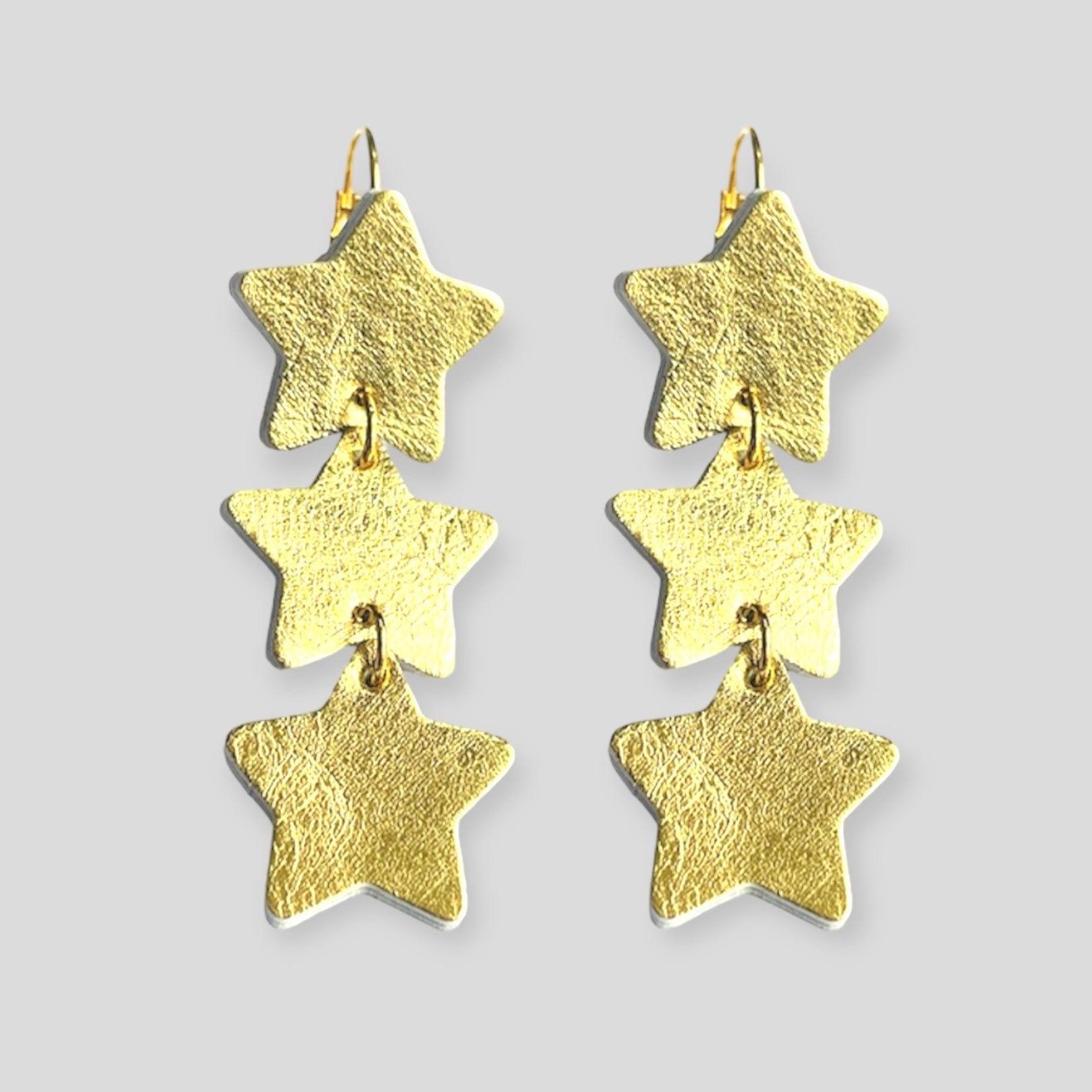 NUNE Boucles d'oreilles Starlight, chapelet d'étoiles en cuir recyclé doré, sur fond gris vues de face