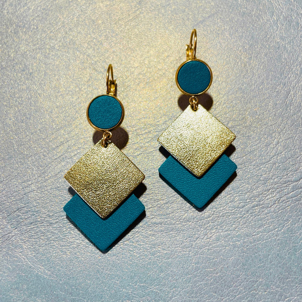 NUNE boucles d'oreilles Adalisa dorées avec cabochon en cuir vert canard et duo de losanges en cuir recyclé vert canard et doré sur fond beige irisé